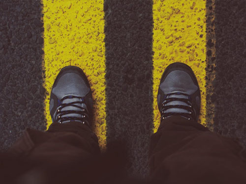 Person standing on yellow pedestrian lane (shoes inside th line)