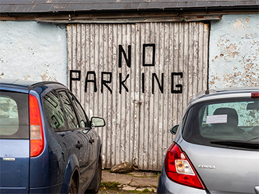 picture of two cars illegally parked in front of a no parking sign