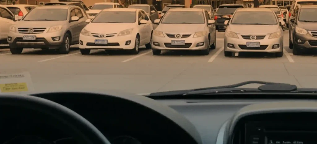 View from inside a car looking at an organized parking lot with several parked vehicles lined up in marked spaces under warm evening light